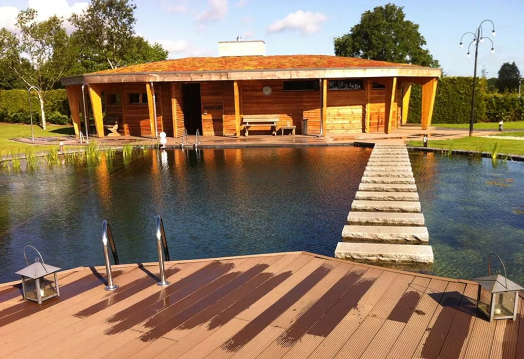 Zwemvijver met stapstenen naar een houten sauna met groen dak
