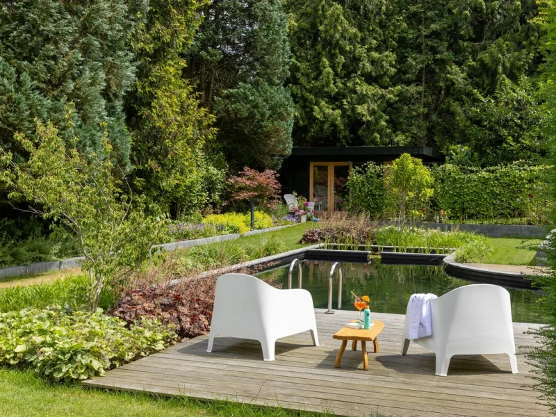 Natuurlijke zwemvijver met houten terras in groene tuin
